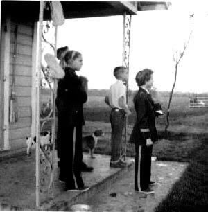 Santleben kids standing on front porch watching a 
crop duster fly through the fields.