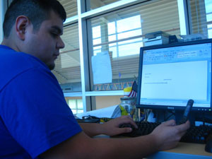 Student Thomas Muese working at a computer and checking his phone for alerts. Photo by Franklin Alvarez